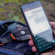 The Motorola Defy on a backpack in the background of someone holding a smartphone using a satellite messaging app.